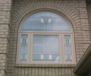 Exterior view of arched window with decorative glass and beige frame on brick home