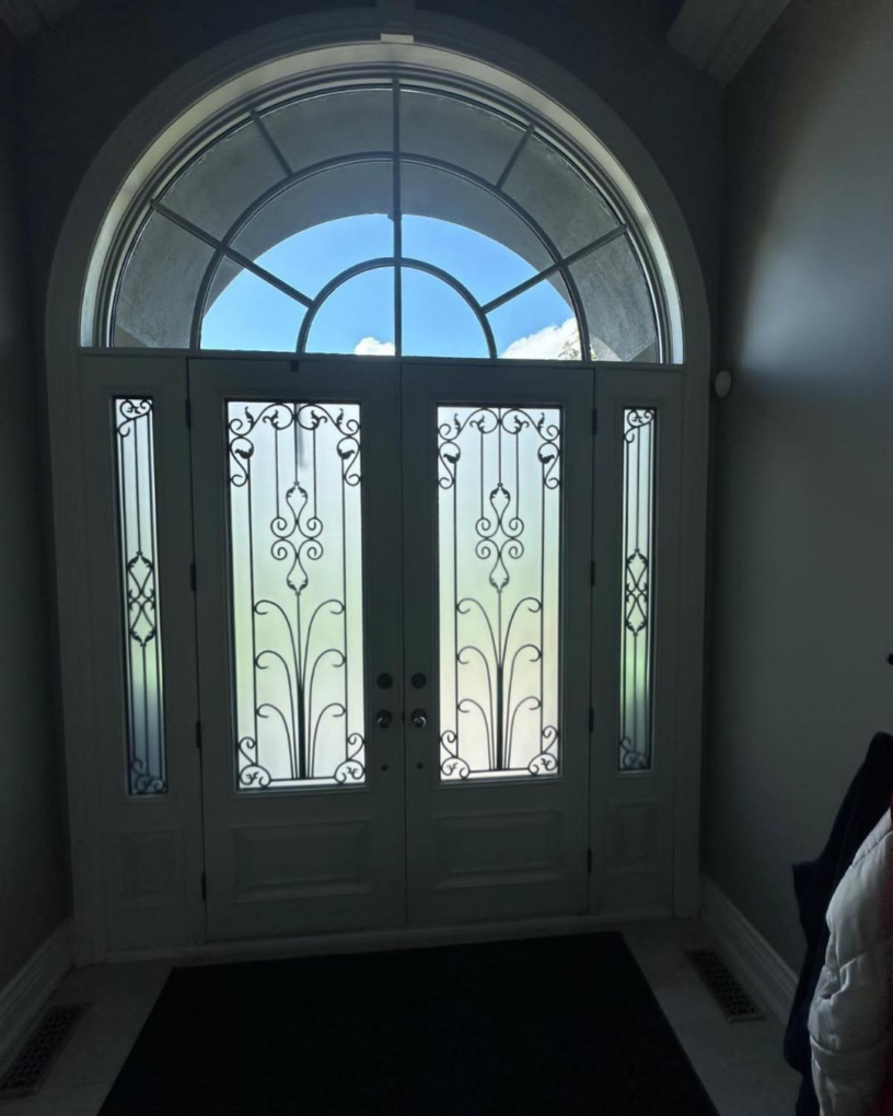 Interior before view of white double doors with ornate glass panels beneath an arched top window