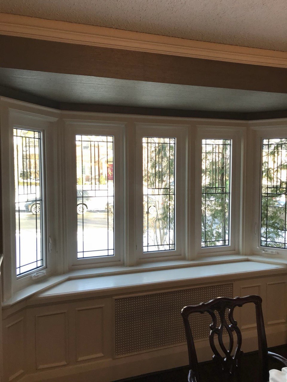 Interior view of the same five-panel bow window with white frames, decorative glass, and a built-in window seat.