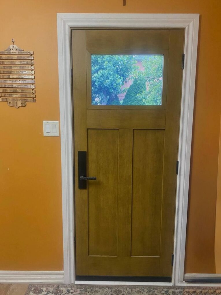 Interior view of a stained wood-grain fiberglass entry door with glass and black hardware in a Bradford home.